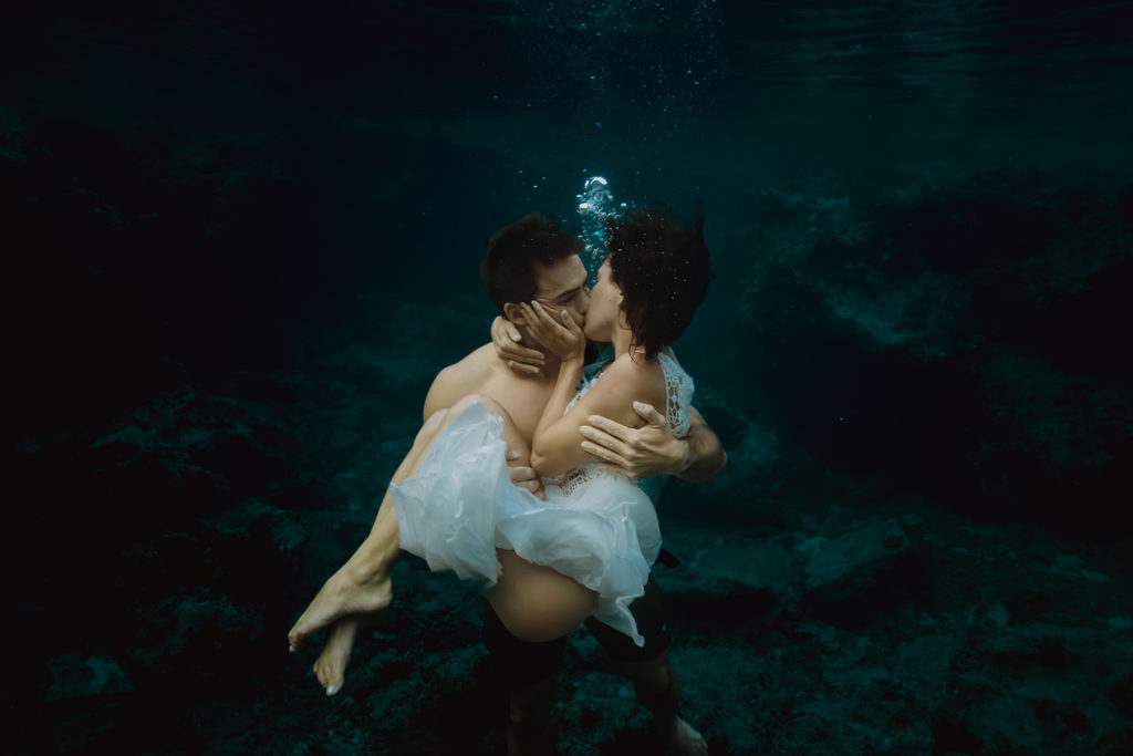 couple floating underwater, kissing to celebrate their beach elopement