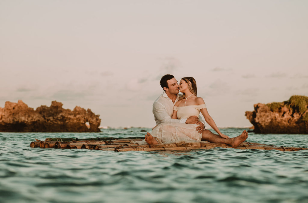 couple sitting on a bamboo raft, cuddling in the sunset after their beach elopement ceremony