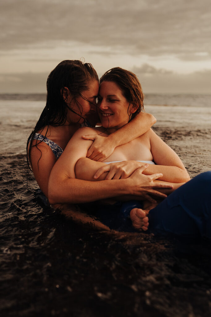 LGBTQ couple hugging on a beach covered by tide water in the sunset light during their pre-wedding photoshoot