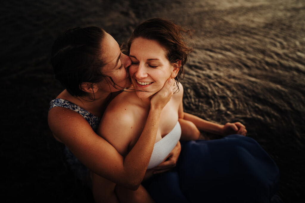 LGBTQ couple hugging and kissing on a beach covered by tide water in the sunset light during their pre-wedding photoshoot